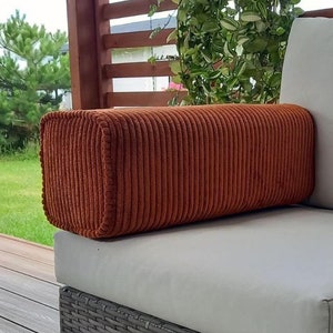 Puede incluir: Un cojín lumbar de pana color óxido con un cojín blanco en una silla de mimbre gris.