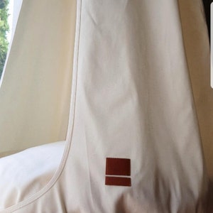 May include: A white canvas hanging chair with a brown leather label. The chair is suspended from the ceiling.