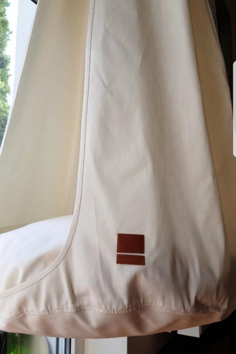May include: A white canvas hanging chair with a brown leather label. The chair is suspended from the ceiling.