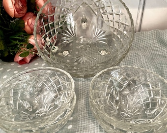 May include: Set of four clear glass bowls with a diamond pattern. The bowls are stacked on top of each other and are sitting on a gray and white patterned surface.
