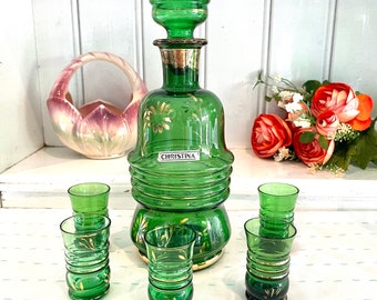 May include: A set of green glass shot glasses and a matching decanter with gold accents. The decanter has the word "CHRISTINA" on it.