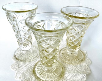 Puede incluir: Tres jarrones de cristal transparente con un patrón de diamante y una base acampanada. Los jarrones están sobre un encaje blanco de ganchillo.