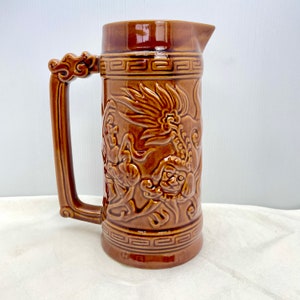 May include: A brown ceramic jug with a dragon design. The jug has a handle and a spout.
