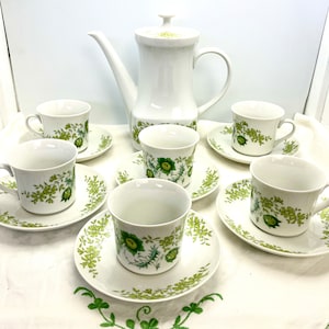 May include: A white porcelain tea set with a green floral pattern. The set includes a teapot, six cups, and six saucers.