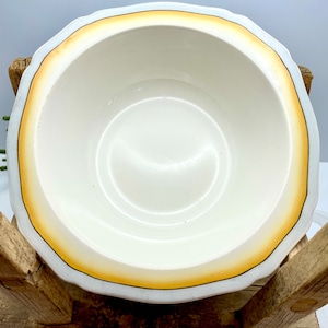 May include: A white ceramic bowl with a scalloped rim and a yellow and brown trim. The bowl is empty.