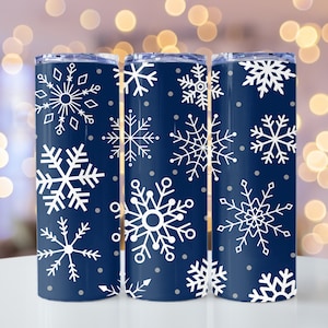 May include: Three navy blue stainless steel tumblers with a white snowflake pattern. The tumblers are lined up in a row on a white surface.