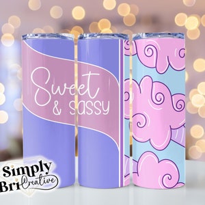 May include: Three stainless steel tumblers with different designs. The first tumbler has a purple and pink ombre design with the text "Sweet & Sassy". The second tumbler has a solid purple design. The third tumbler has a light blue background with pink clouds.