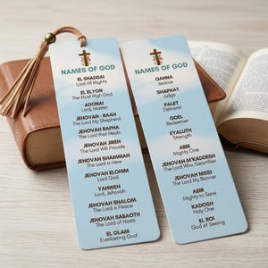 Könnte beinhalten: Zwei vertikale Lesezeichen mit dem Text "NAMEN GOTTES" und einer Liste von Namen und Titeln. Die Lesezeichen sind hellblau mit einem Kreuz und floralem Design oben. Ein braunes Lederbuch und eine Quaste befinden sich im Hintergrund.