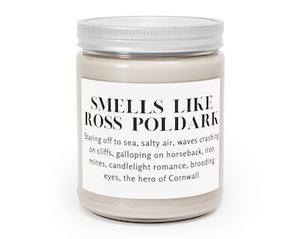 May include: A brown glass candle jar with a silver lid. The label reads "Smells Like Ross Poldark" and includes a description of the scent: "Staring off to sea, salty air, waves crashing on cliffs, galloping on horseback, iron mines, candlelight romance, brooding eyes, the hero of Cornwall."