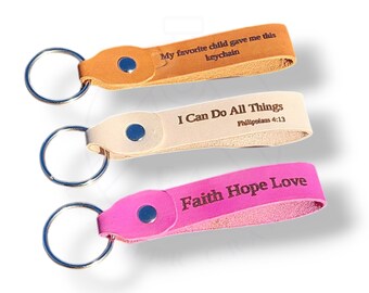 May include: Three leather keychains in tan, cream, and pink. The tan keychain reads "My favorite child gave me this keychain." The cream keychain says "I Can Do All Things" and the pink one says "Faith Hope Love."