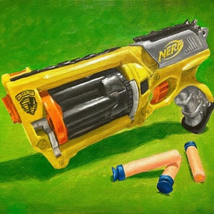 May include: A yellow and gray toy gun with the word "NERF" printed on it. The gun is lying on a green surface with two orange and blue darts next to it.