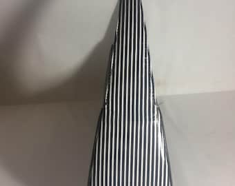 Puede incluir: Un bolso a rayas blancas y negras con una forma estrecha y alargada. El bolso presenta rayas verticales y un acabado brillante. El asa también está rayada. El bolso está de pie.