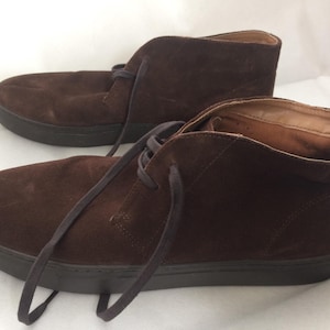 Puede incluir: Un par de botines chukka de ante marrón con suelas marrón oscuro y cordones a juego. Las botas tienen un diseño clásico, adecuado para uso informal. El material de ante les da un aspecto suave y texturizado.