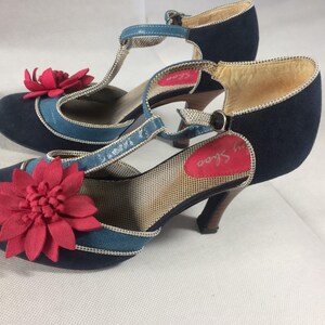 Puede incluir: Un par de zapatos azul marino con correa en T y un adorno de flor roja. Los zapatos tienen un ribete azul turquesa y un tacón pequeño. La plantilla tiene el texto "My Shoe".