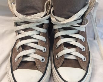 Puede incluir: Un par de zapatillas altas de lona en color marrón apagado. Las zapatillas tienen cordones blancos, puntera de goma blanca y suela blanca con una franja negra. Diseñadas para uso casual.