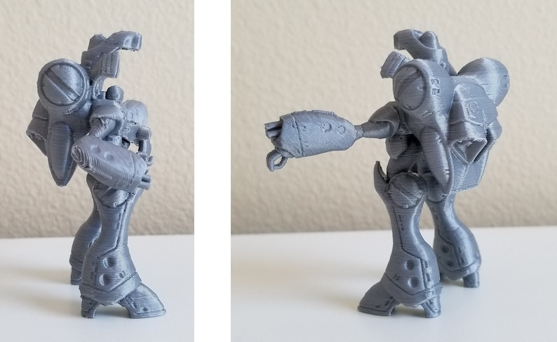 May include: A gray 3D printed robot figurine with a detailed design. The robot has a large head with a single eye and a long, articulated arm.