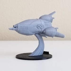 May include: A gray 3D printed spaceship model on a black base. The spaceship has a long, pointed nose and two engines on the back.