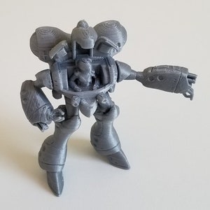May include: A gray 3D printed robot toy with a detailed design. The robot has a cockpit, two arms, and two legs.