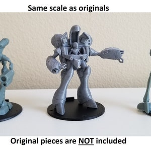 May include: Three 3D printed gray robot figurines on black bases. The robots are different sizes and have different designs.  "Same scale as originals" and "Original pieces are NOT included" are printed below the robots.