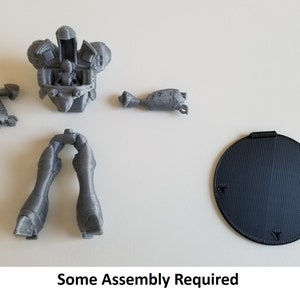May include: A gray 3D printed model of a robot with multiple parts, including a torso, legs, arms, and a base. The parts are separate and require assembly. The text "Some Assembly Required" is printed below the image.
