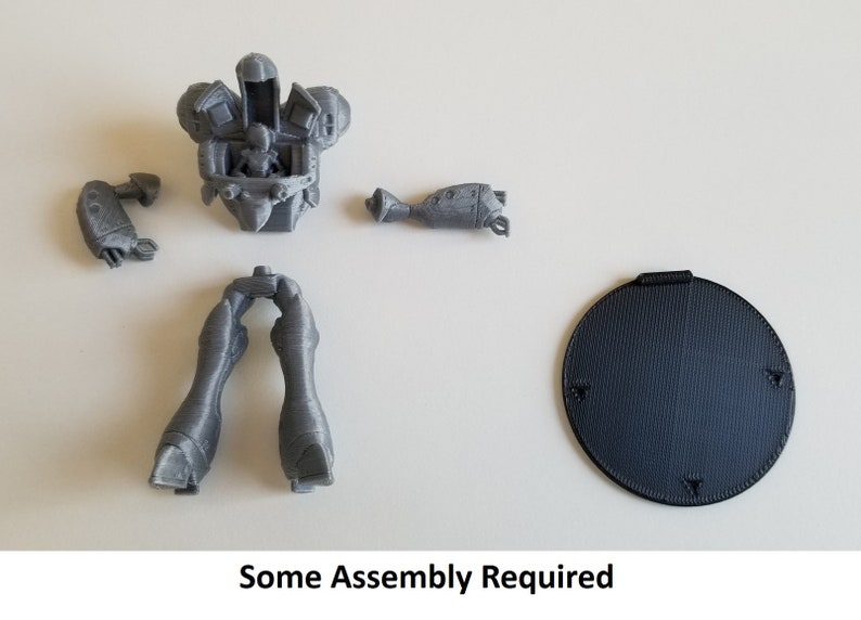 May include: A gray 3D printed model of a robot with multiple parts, including a torso, legs, arms, and a base. The parts are separate and require assembly. The text "Some Assembly Required" is printed below the image.