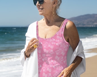 May include: A woman wearing a pink floral swimsuit with a white shawl on the beach.