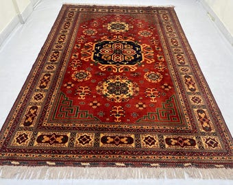 May include: A rectangular, hand-knotted rug with a deep red field and intricate geometric patterns in gold, black, and green. The rug features a central medallion and a detailed border with fringe along the edges. This traditional rug is suitable for living rooms and bedrooms.