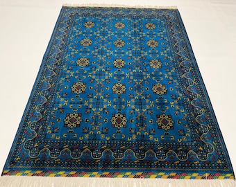 May include: A rectangular area rug featuring a vibrant blue background with a repeating pattern of dark geometric squares and small yellow floral motifs. The rug is framed by a dark border with intricate patterns and finished with white fringe.
