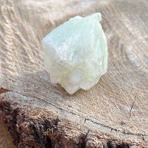 May include: A cluster of pale green crystals with a rough, textured surface. The crystals are arranged in a pyramid shape and have a translucent appearance.