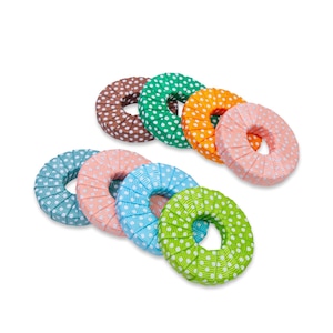 Könnte beinhalten: Eine Sammlung farbenfroher, donut-förmiger Stoffringe. Die Ringe sind in verschiedenen Farben erhältlich, darunter Braun, Grün, Orange, Rosa, Blau und Grün, jeweils mit weißen Punkten. Der Stoff ist plissiert, was den Ringen ein strukturiertes Aussehen verleiht. Die Ringe sind auf weißem Hintergrund angeordnet.