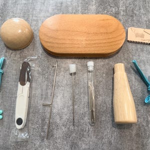 May include: A collection of craft tools and accessories, including a wooden oval box, a wooden ball, a wooden bottle-shaped item, and a small wooden card with text. Other items include a pair of scissors, needles, and blue cord.