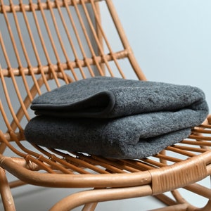 Peut inclure: Une couverture grise pliée reposant sur une chaise en osier brun clair.
