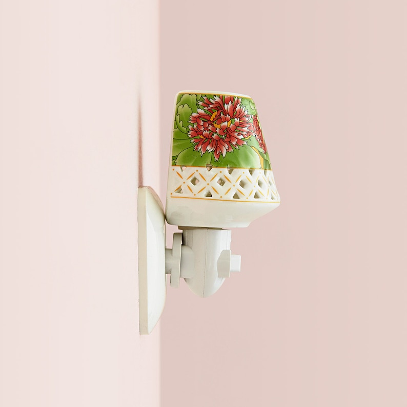 K&ouml;nnte beinhalten: Ein wei&szlig;es, an der Wand montiertes, steckbares Nachtlicht aus Keramik mit floralem Design. Der Schirm hat ein gr&uuml;nes und wei&szlig;es Gittermuster mit einer roten und pinkfarbenen Blume.
