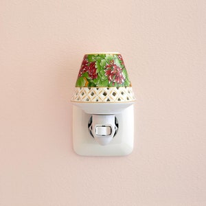 K&ouml;nnte beinhalten: Ein wei&szlig;es, steckbares Nachtlicht aus Porzellan mit einem Blumendesign. Das Nachtlicht hat einen wei&szlig;en Schalter und ist in eine Steckdose gesteckt.