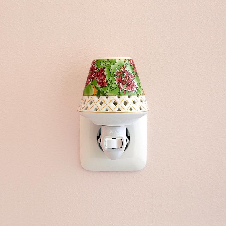 K&ouml;nnte beinhalten: Ein wei&szlig;es, steckbares Nachtlicht aus Porzellan mit einem Blumendesign. Das Nachtlicht hat einen wei&szlig;en Schalter und ist in eine Steckdose gesteckt.