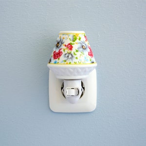 Pu&ograve; includere: Un lumino notturno in ceramica bianca con un design floreale in tonalit&agrave; di rosso, blu e verde. Il lumino notturno &egrave; collegato a una presa di corrente bianca.