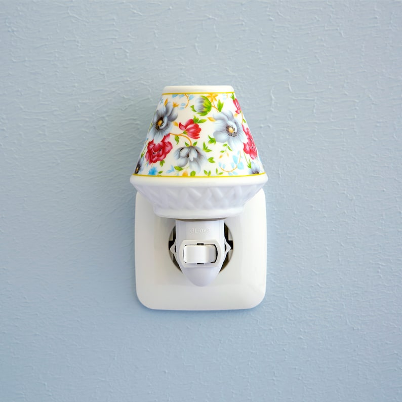 Pu&ograve; includere: Un lumino notturno in ceramica bianca con un design floreale in tonalit&agrave; di rosso, blu e verde. Il lumino notturno &egrave; collegato a una presa di corrente bianca.