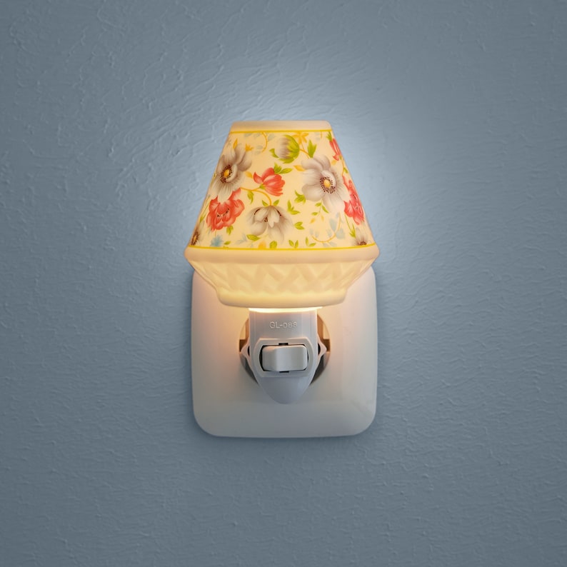 Pu&ograve; includere: Un'abat-jour da notte in ceramica bianca con un motivo floreale. La luce notturna &egrave; collegata a una presa di corrente e ha un interruttore laterale.
