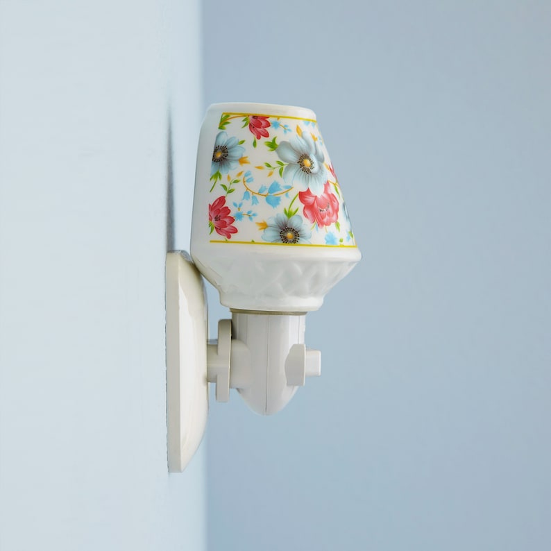 Pu&ograve; includere: Un lampadario da parete in ceramica bianca con un motivo floreale. Il lampadario ha un cavo bianco e una spina bianca.