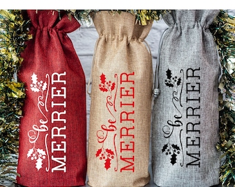 May include: Three burlap wine bottle gift bags with the text "Oh, be merrier" in red, white, and black lettering. The bags are decorated with holly leaves and berries.