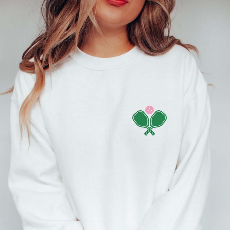 May include: White sweatshirt with a green pickleball paddle and pink ball graphic.