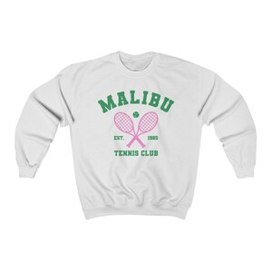 K&ouml;nnte beinhalten: Wei&szlig;er Pullover mit einem gr&uuml;nen und rosafarbenen Grafikdesign. Die Grafik zeigt "Malibu Tennis Club" mit einem Tennisschl&auml;ger und einem Ball.