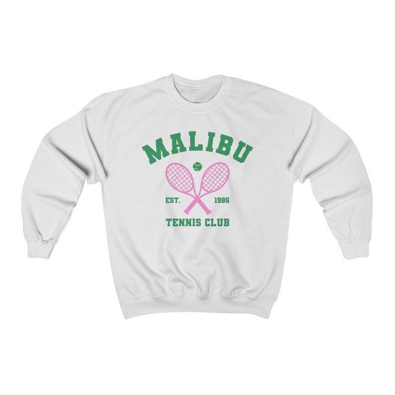 K&ouml;nnte beinhalten: Wei&szlig;er Pullover mit einem gr&uuml;nen und rosafarbenen Grafikdesign. Die Grafik zeigt "Malibu Tennis Club" mit einem Tennisschl&auml;ger und einem Ball.