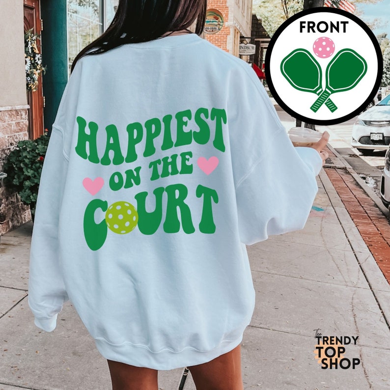 May include: Light blue sweatshirt with the text "Happiest on the Court" in green letters with a green pickleball and pink hearts.