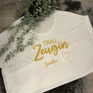 May include: White t-shirt with gold lettering that says "Trau Zeugin" and "Sandra" with a small heart.
