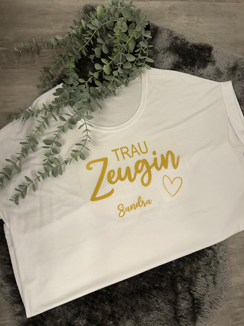 May include: White t-shirt with gold lettering that says "Trau Zeugin" and "Sandra" with a small heart.