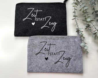 Könnte beinhalten: Zwei Filz-Reißverschlusstaschen, eine dunkelgraue und eine hellgraue, werden gezeigt. Jede Tasche trägt den Schriftzug "Zeit statt Zeug" in weißer Schrift, mit einem kleinen Herz. Die Taschen sind rechteckig und haben schwarze Reißverschlüsse.
