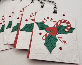 May include: Five white gift tags with red and green holly and candy cane designs. The tags are tied with black and white twine.