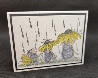 May include: A greeting card featuring three mice wearing yellow flowers as umbrellas in the rain. The card has a black border.