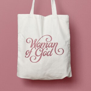 May include: A white canvas tote bag with the words "Woman of God" printed in pink cursive lettering.